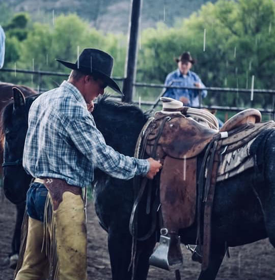 Zach Curran saddling up a colt at the Bartlett Ranch with one of his Keith Valley Saddles while Bill Smith watches on in the background.